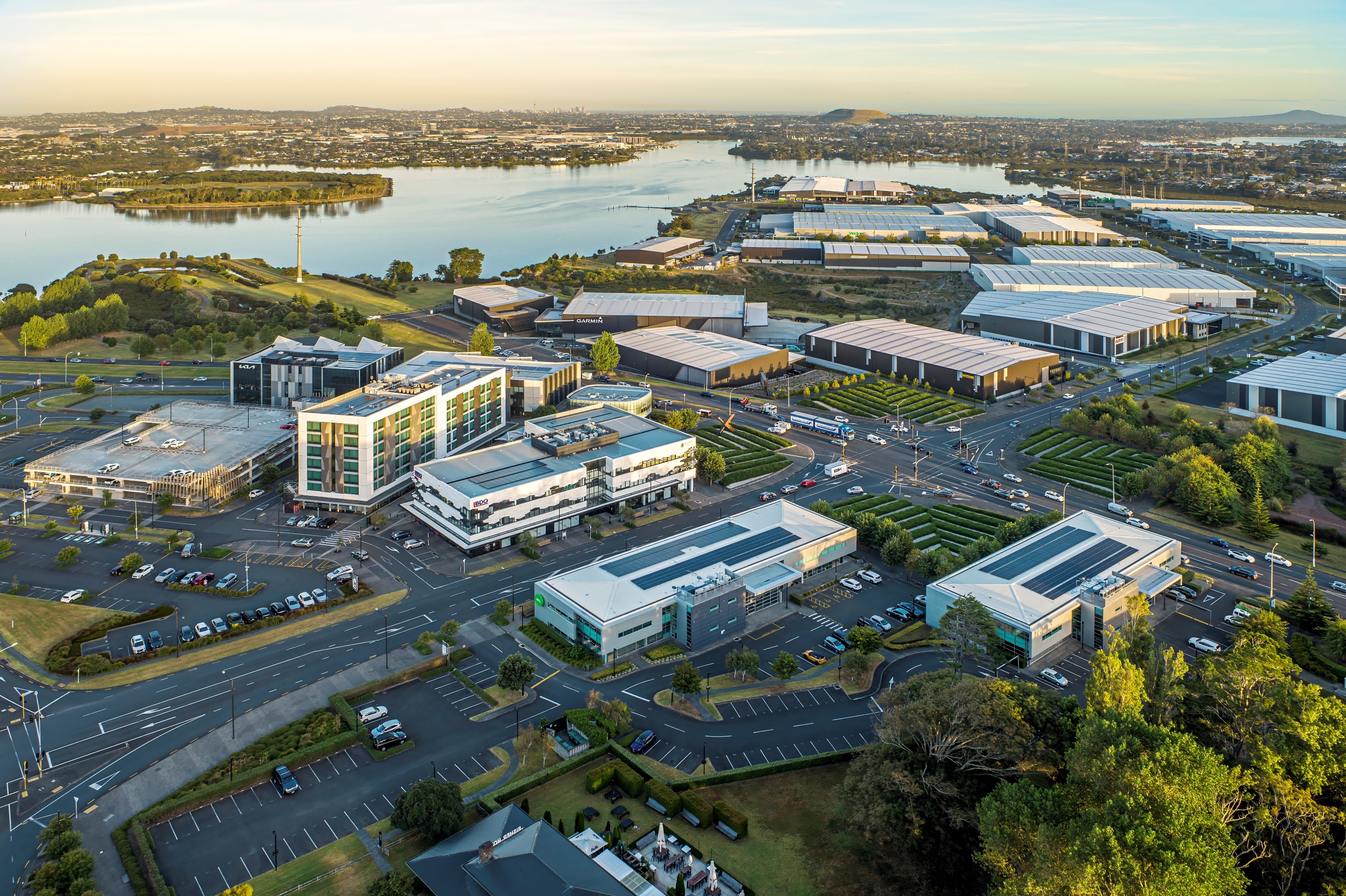 Aerial view of a modern business park with office buildings, roads, parking lots, and a river in the background.