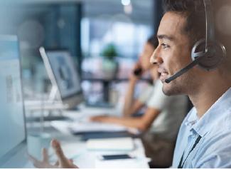 Man wearing headset speaking while working on computer in an office setting.