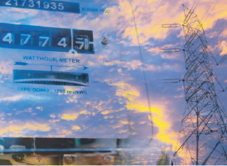 Electric meter reading 47457 with a sunset sky and power transmission tower in the background.