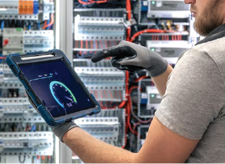 Technician in gray shirt and gloves holds tablet showing network speed test in server room.
