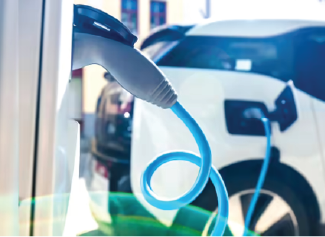 Close-up of an electric vehicle charging cable plugged into a white car at a charging station.