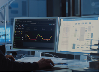 Dual monitors showing data analytics with charts and graphs on a desk in a dimly lit office.