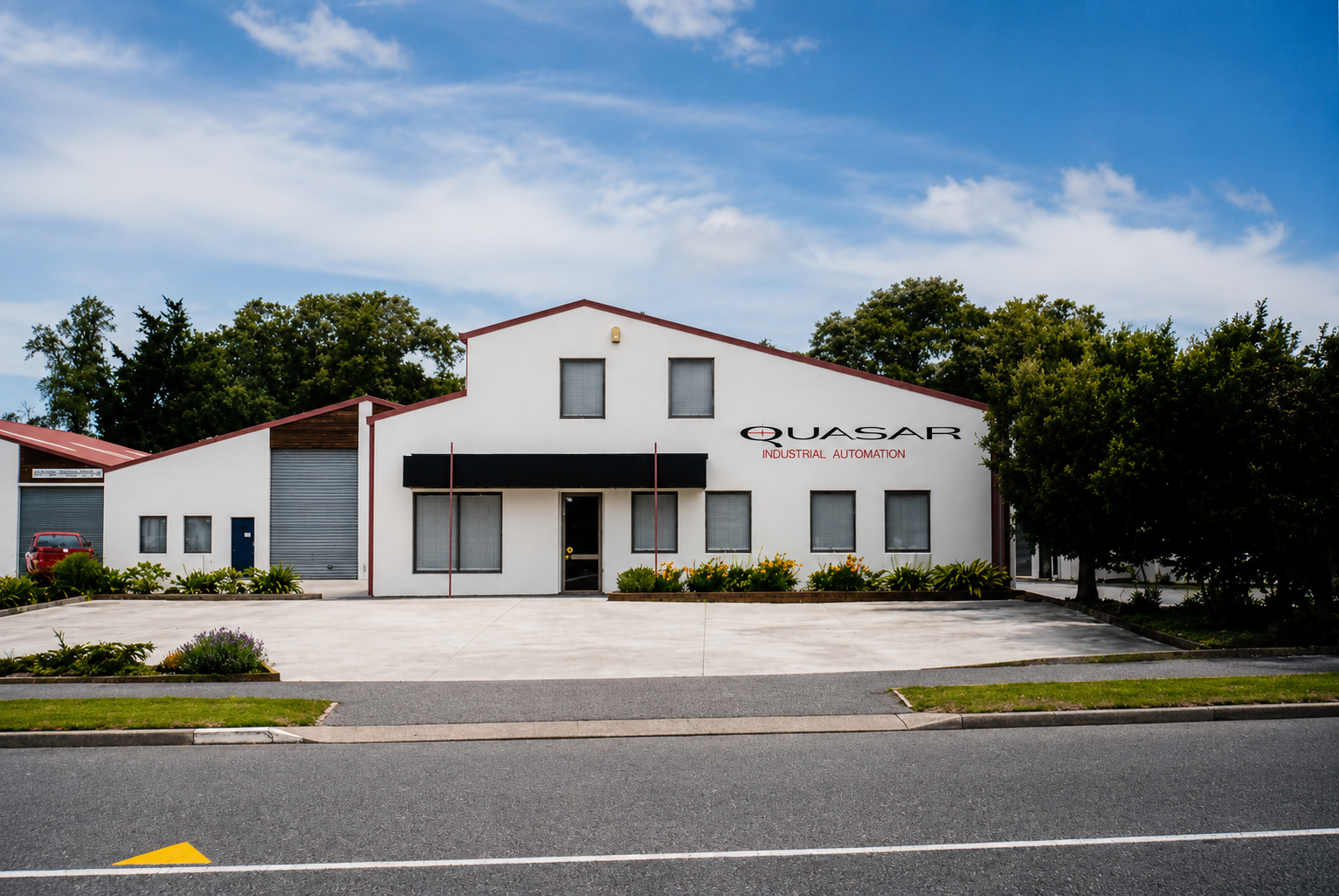 White industrial building with QUASAR INDUSTRIAL AUTOMATION sign and parking in front under blue sky.