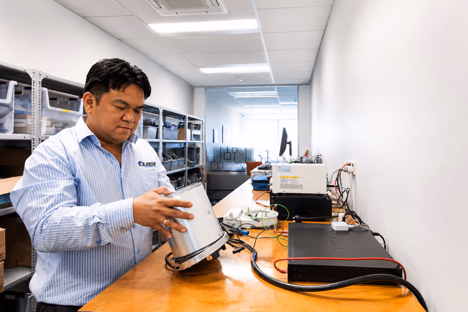 Man in striped shirt working with electronic equipment on a wooden bench in a lab.