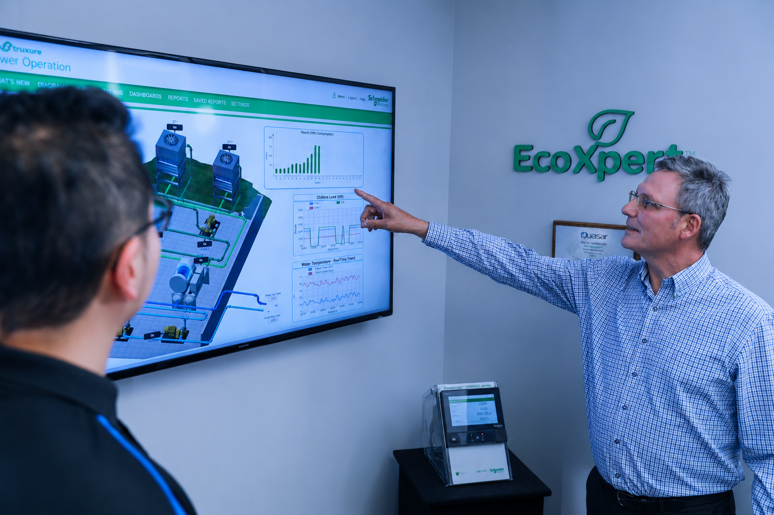Older man points at data charts on wall screen while younger man watches in an office with EcoXpert sign.
