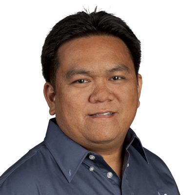 Portrait of a man with short black hair wearing a dark blue collared shirt against a gray background.