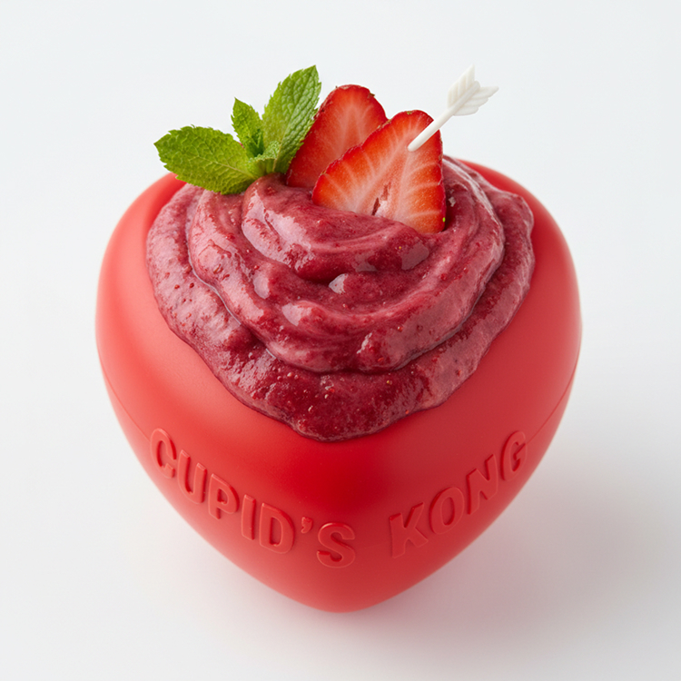 Red heart-shaped Cupid's Kong dog toy topped with a swirl of red frozen treat, sliced strawberries, and a sprig of fresh mint.