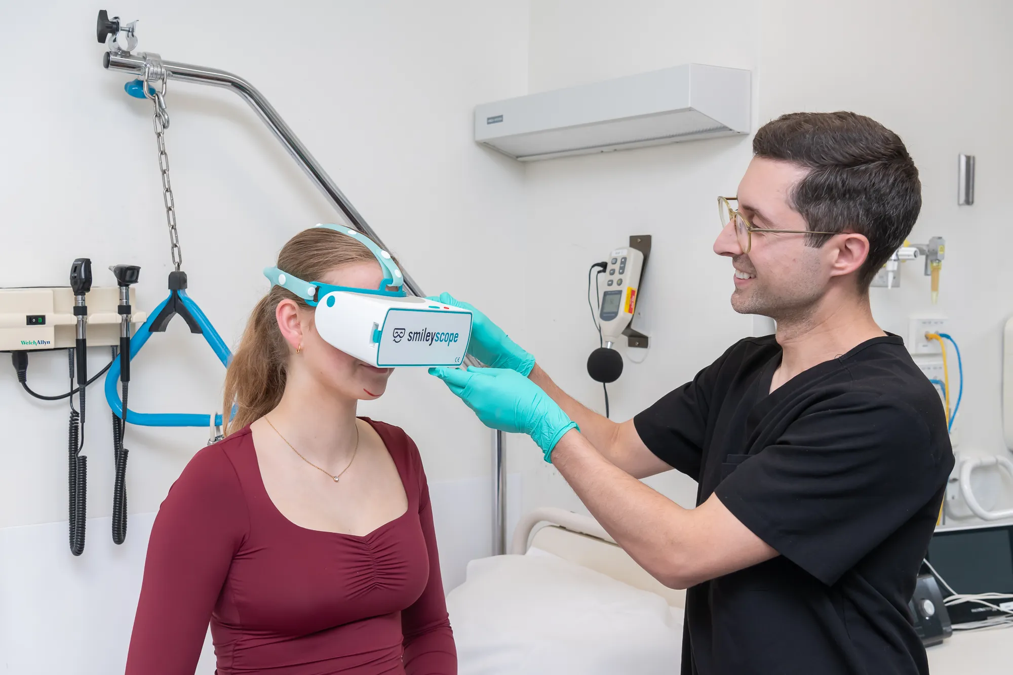 Healthcare professional adjusting a smileyscope VR headset on a patient in a clinical room.