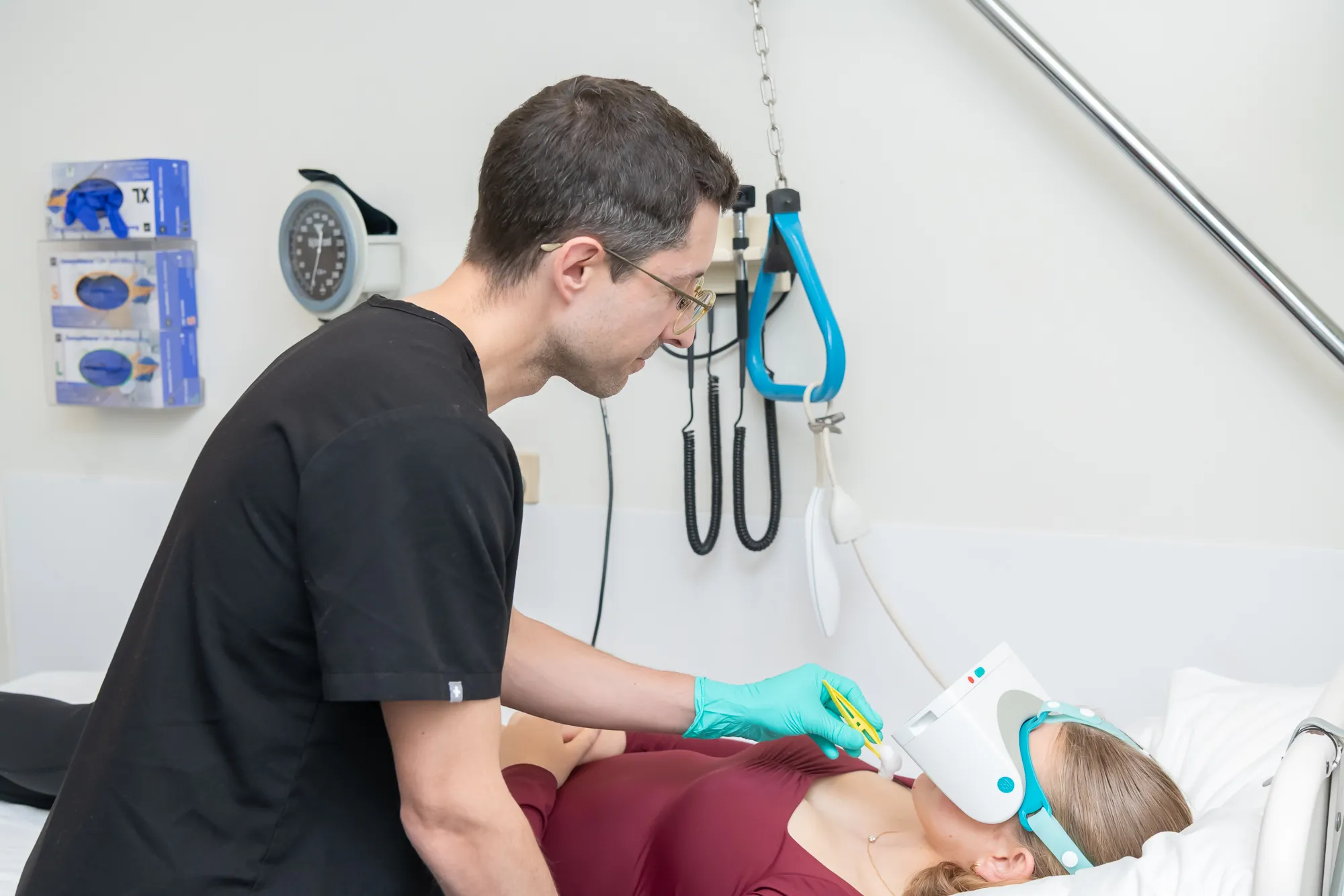 Medical professional wearing gloves administering eye treatment to a patient lying in a hospital bed with a specialized eye device.