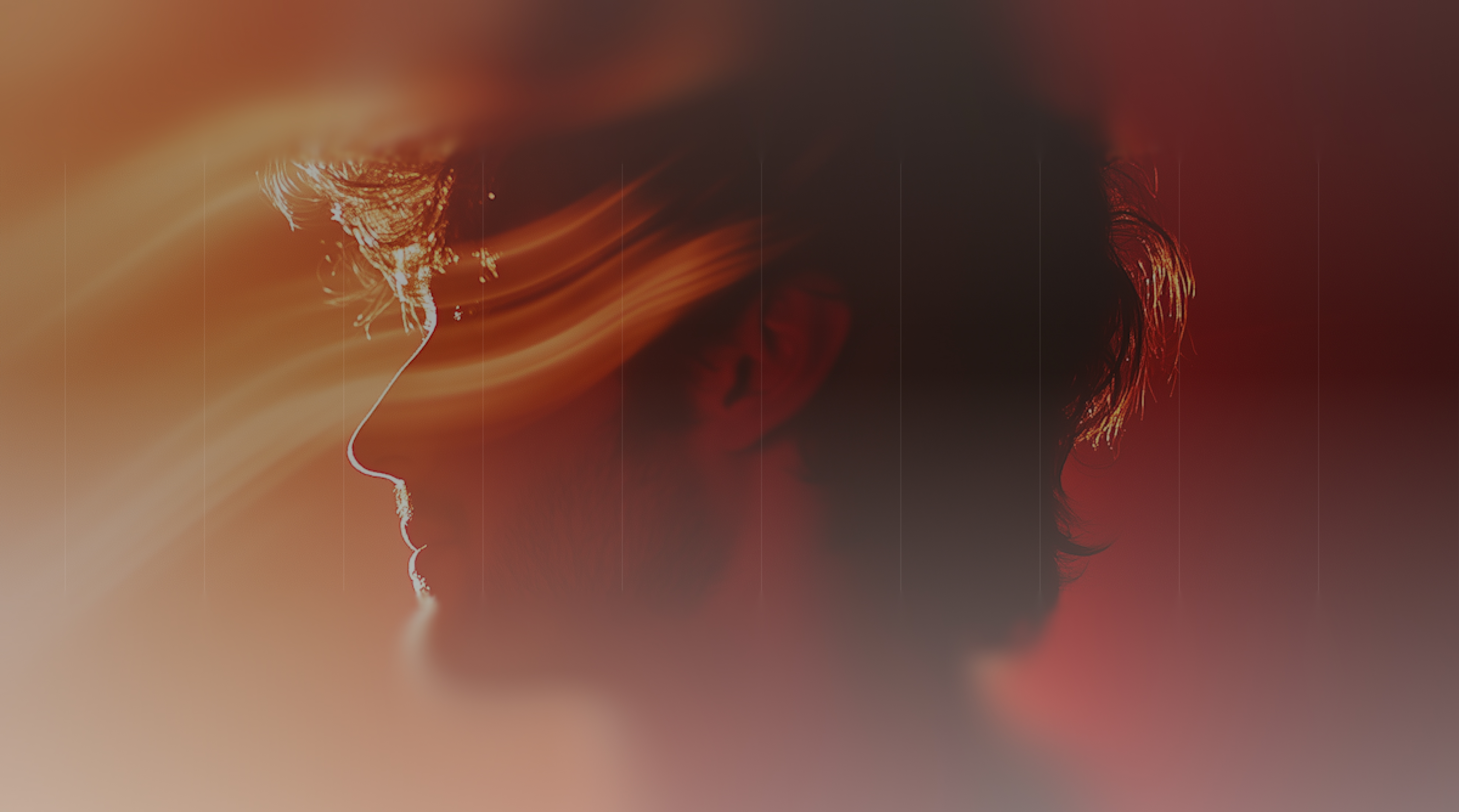 Side profile of a young man with curly hair illuminated by warm, flowing light streaks against a dark blurred background.