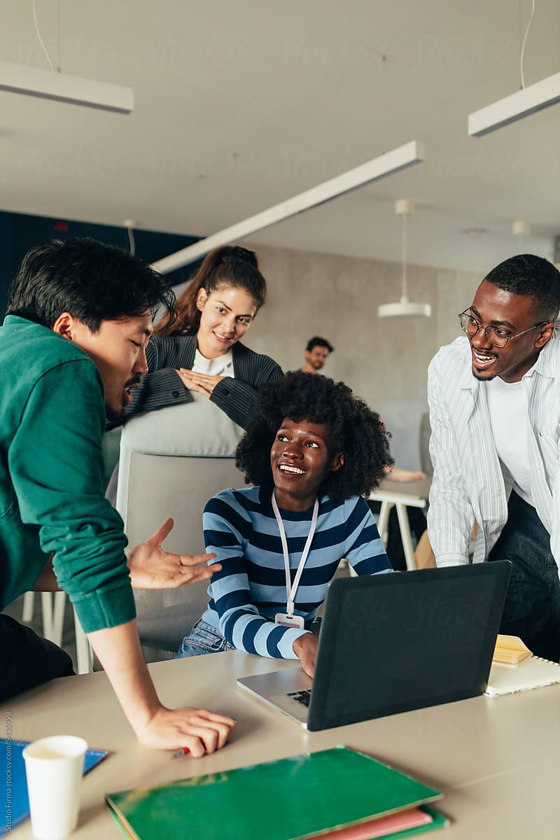 Four colleagues gathered around a laptop at an office desk, talking