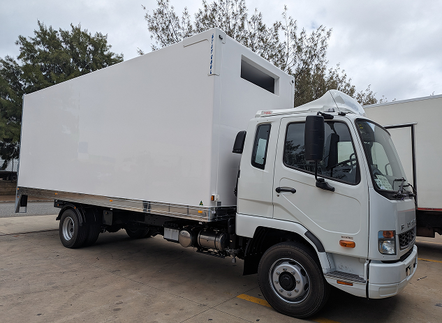 White box truck parked on concrete with trees and cloudy sky in the background.
