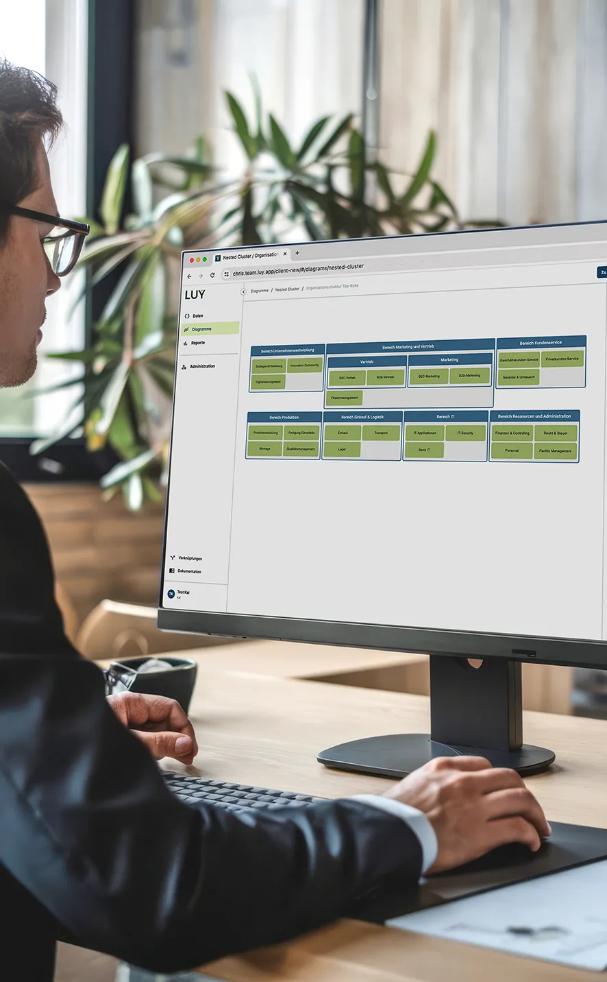 Ein Mann mit Brille arbeitet an einem Computer mit einem Organisationsdiagramm auf dem Bildschirm in einem modernen Büro.