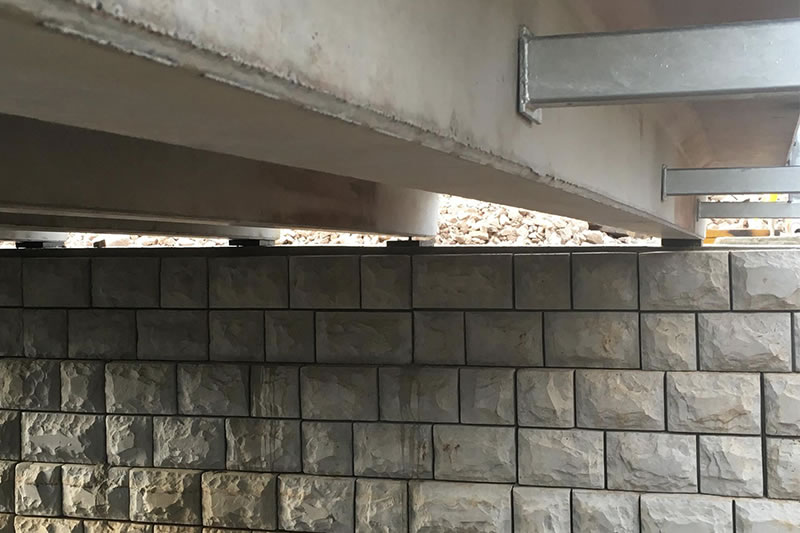 Close-up of a concrete bridge section above a wall made of large rectangular stone blocks.