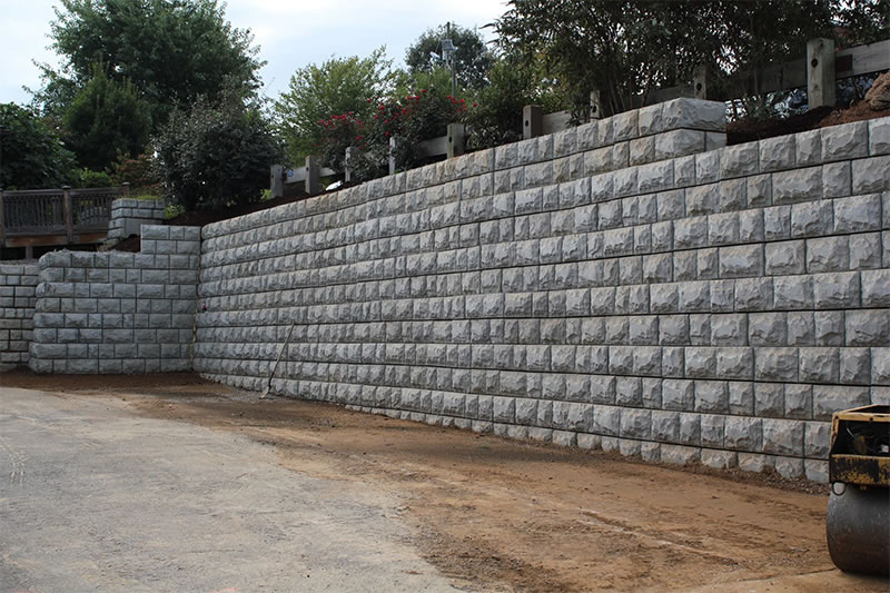 Large retaining wall made of gray stone blocks with a garden and trees above it.