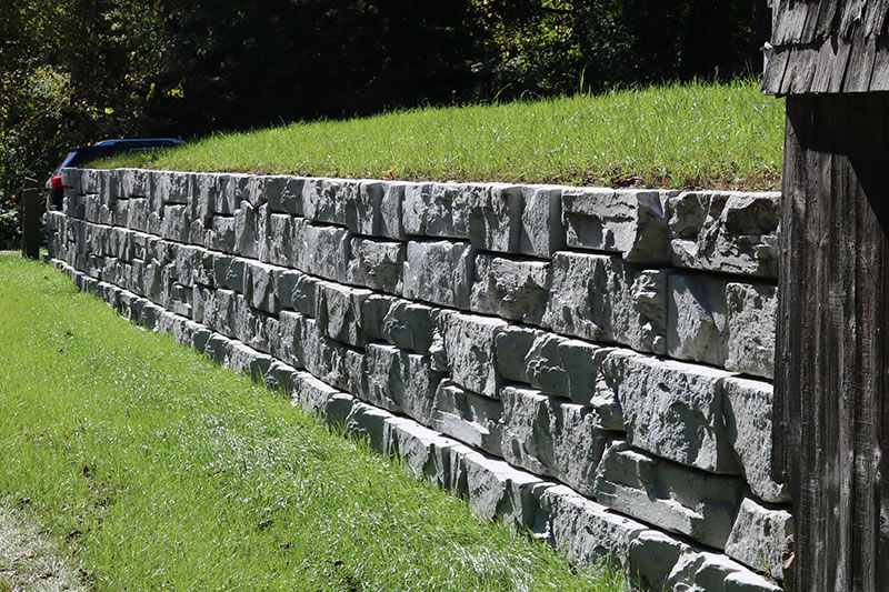 Long stone retaining wall with a grassy top and a wooden structure partially visible on the right side.