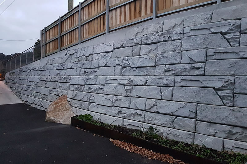 Stone retaining wall with rectangular block pattern alongside paved pathway and small garden bed.