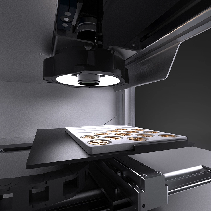 Close-up of a high-tech 3D printer nozzle illuminating a build platform with multiple small circular print sections.