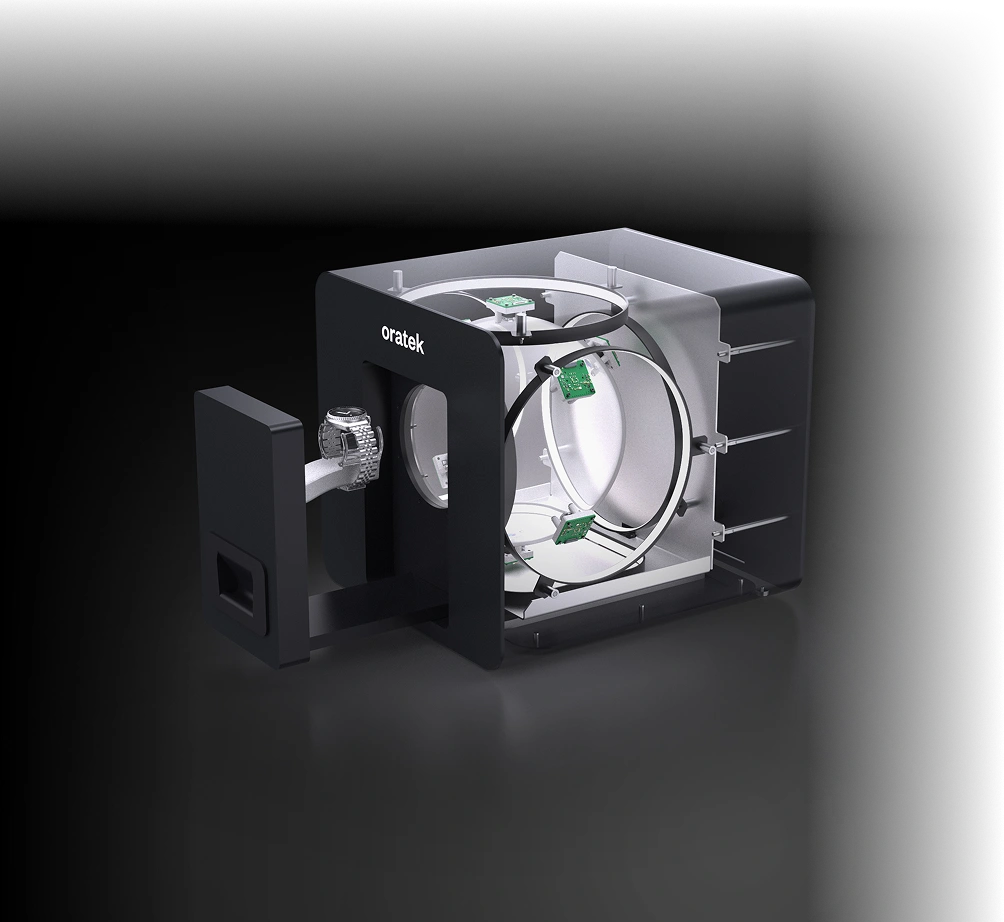 Black smartwatch placed on a holder, positioned inside an open black and transparent cube device labeled 'oratek,' showing internal green circuit components.