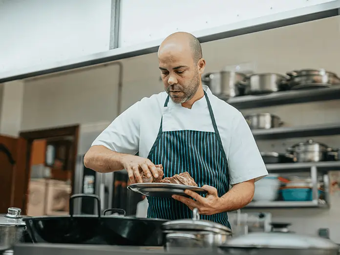 Chef in striped apron works in restaurant kitchen, preparing dishes accurately with guidance from a kitchen display system.