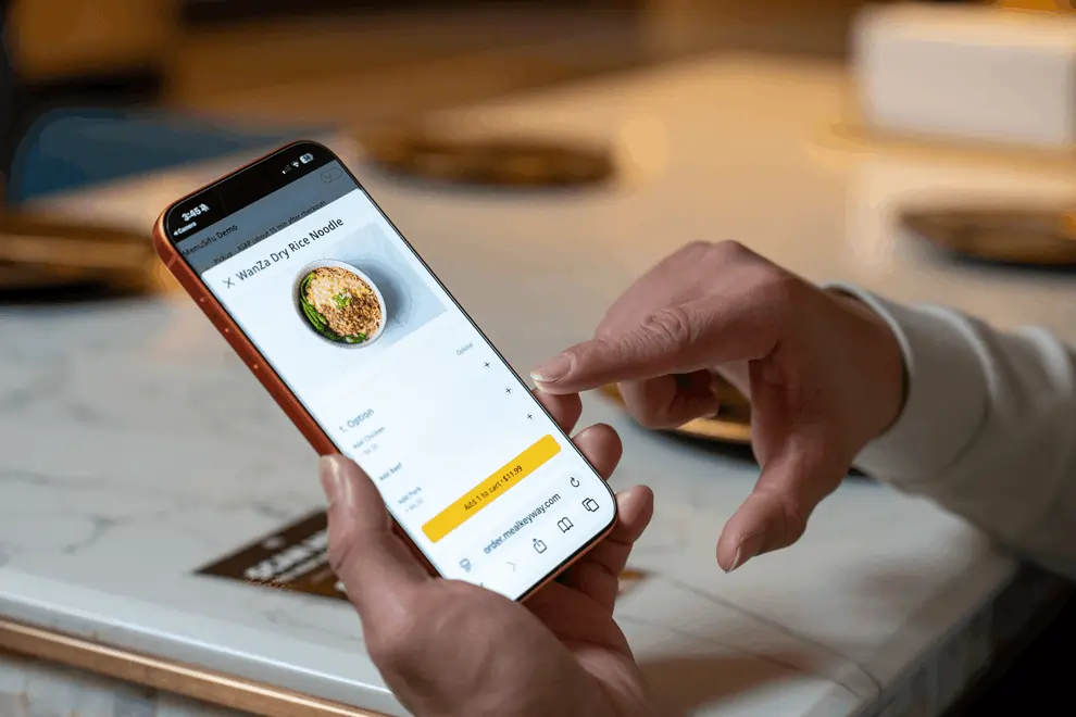 Guest using smartphone to order noodles from a digital restaurant menu after scanning a QR code on the table.
