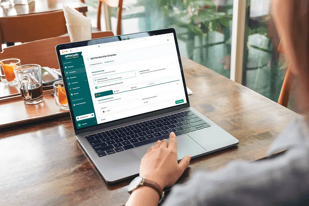 Restaurant staff editing membership campaign using a loyalty program dashboard on a laptop at a café table.