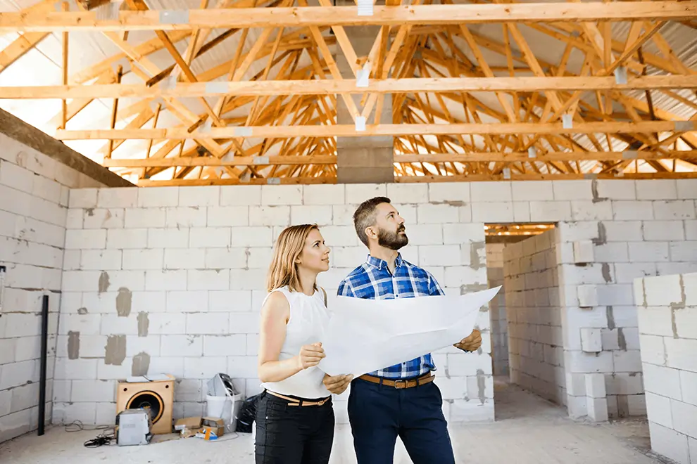 Man and woman reviewing construction plans inside unfinished building, planning project or discussing financing options.