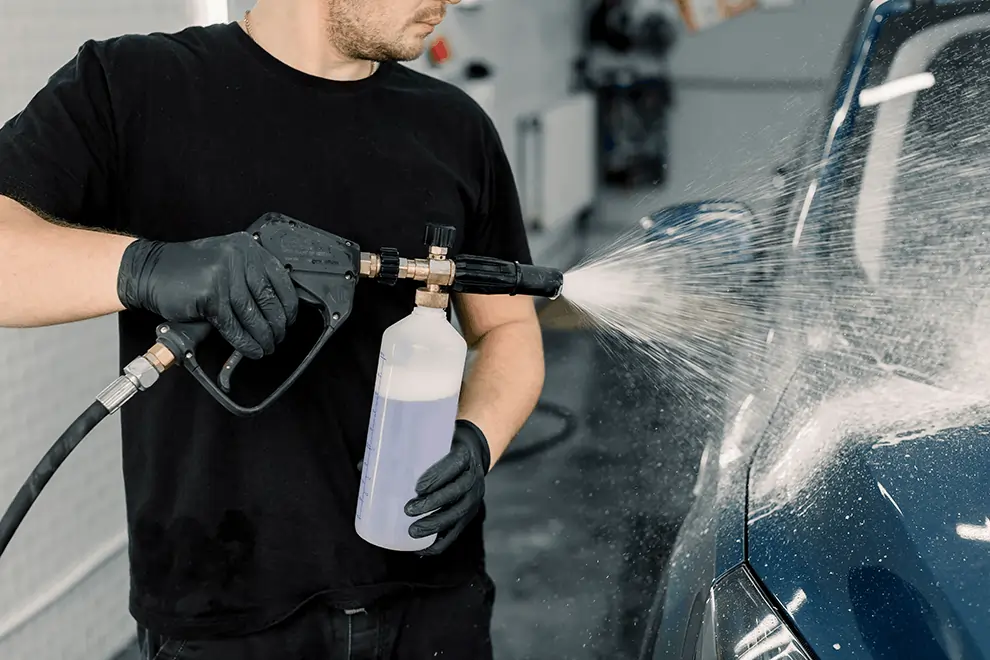 Close-up of a worker cleaning a car with a high-pressure foam spray gun.