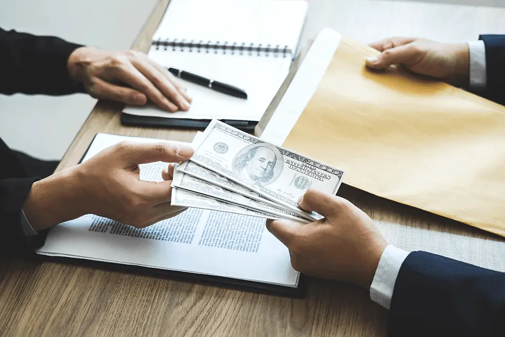 Cash handoff during a small business loan agreement, with documents and an envelope on the meeting table.