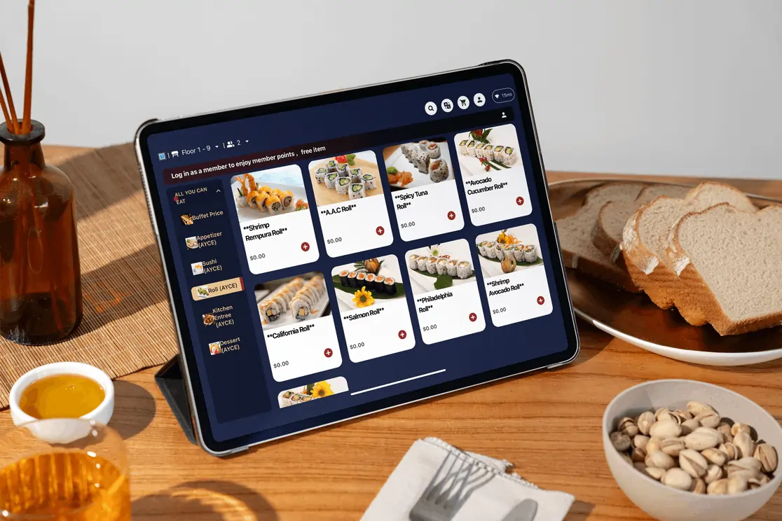 Restaurant e-menu tablet with sushi selection, placed on a wooden table next to sliced bread and a bowl of pistachios.