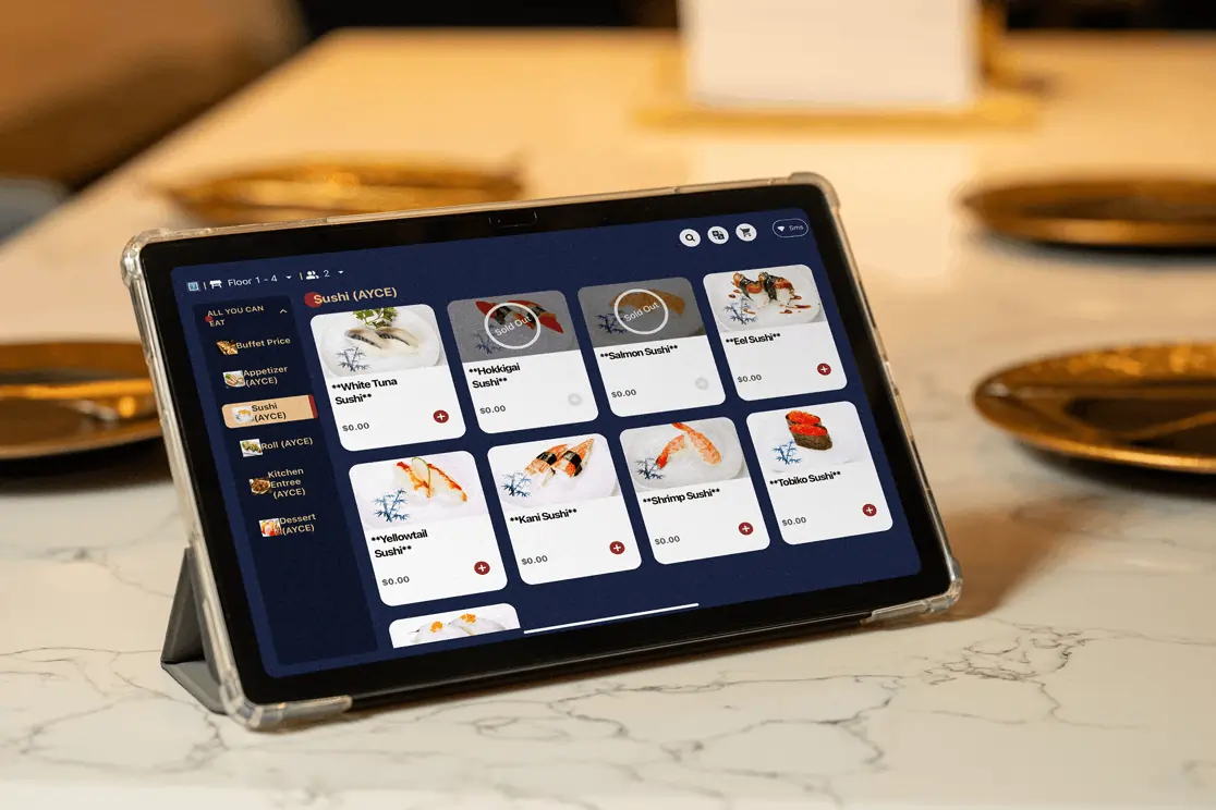 Tablet displaying a digital sushi menu on a restaurant table with plated settings in the background.