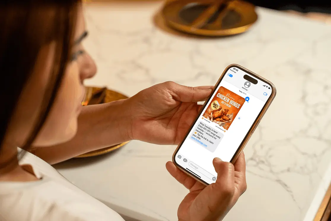 A guest reads a restaurant promo SMS offering 50% off wings, boosting repeat visits with a loyalty program reminder.