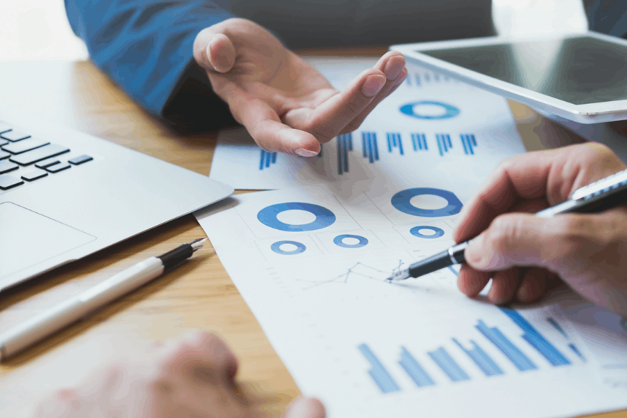 Business professionals analyzing charts and graphs during a data strategy meeting with a laptop and tablet on the table.