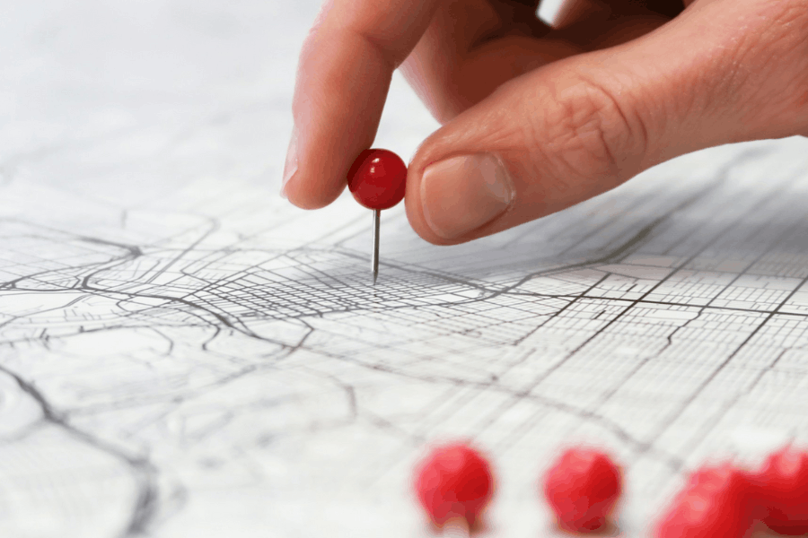 Hand placing a red pin on a map to mark a local market location, representing strategic planning for regional business expansion.