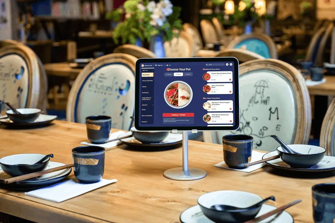 Tablet-based self-ordering screen on restaurant table with detailed hotpot soup base menu and place settings for multiple guests.