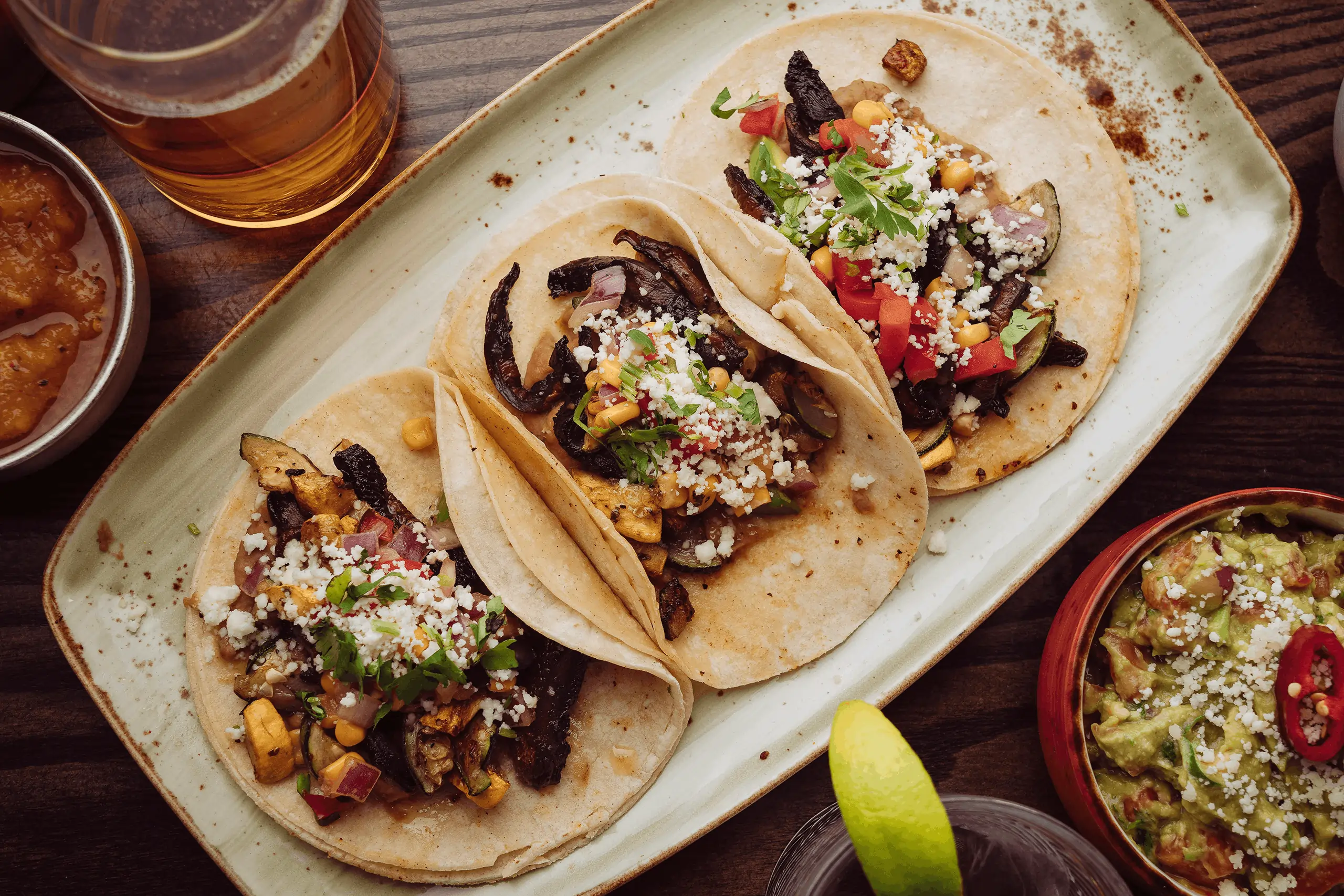 Three veggie tacos topped with cheese and cilantro next to guacamole and salsa, ordered using Mexican restaurant POS system tools.