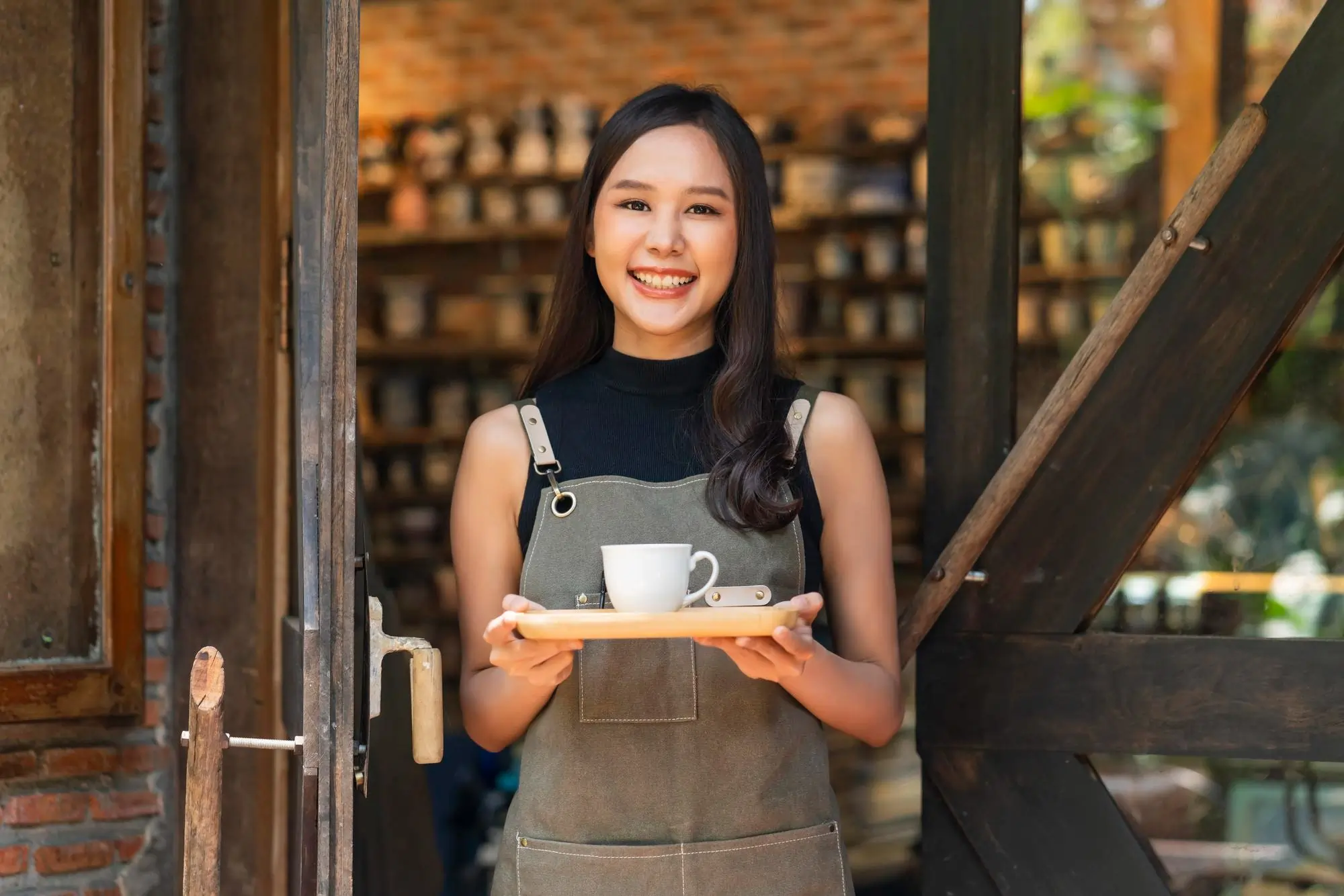 Happy server at a Thai café smiles with a coffee tray, praising the ease of use and speed of her Thai restaurant POS system.