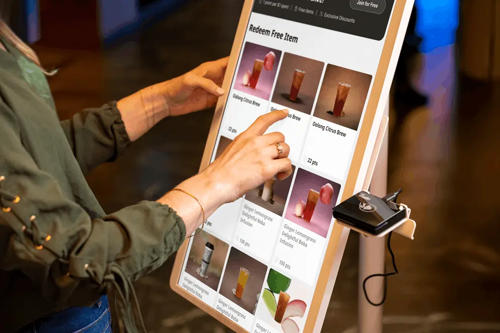 Customer selects a drink reward on a self-ordering kiosk at a quick service restaurant to speed up ordering.