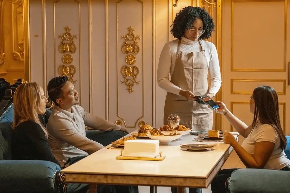 Tableside mobile payment completed with contactless tap as server stands beside seated guests in luxury restaurant.