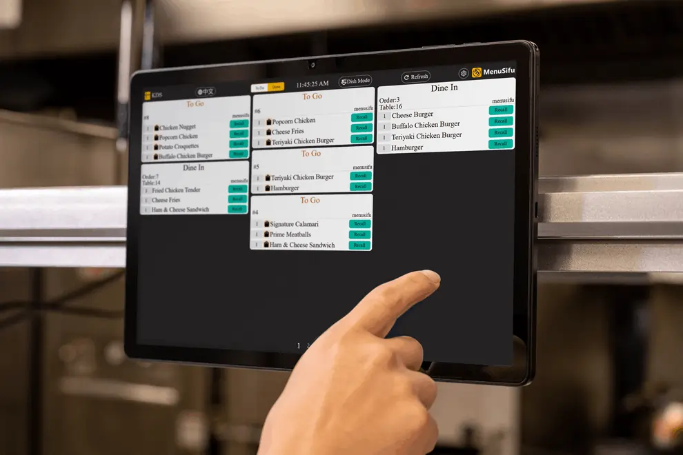 Kitchen staff using KDS screen to manage dine-in and to-go orders in a busy restaurant kitchen.