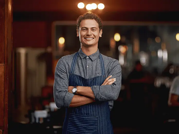 Smiling restaurant owner stands confidently in dining room showcasing success powered by a full service restaurant pos system.