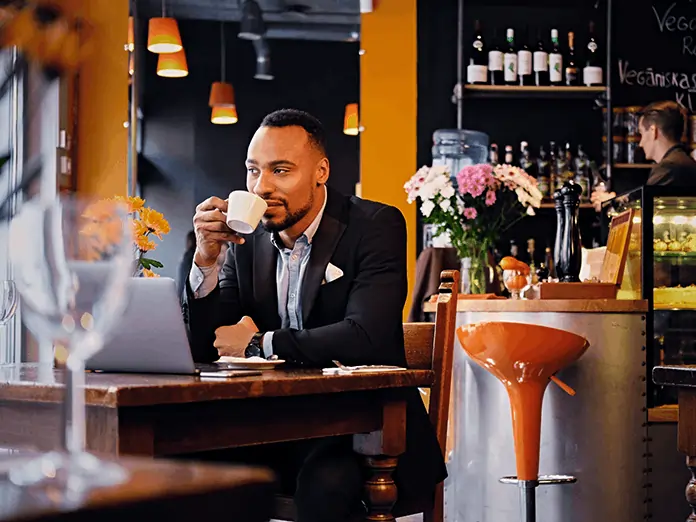 Cafe owner review sales on laptop while enjoying coffee showing streamlined operations with full-service-restaurant-pos-system