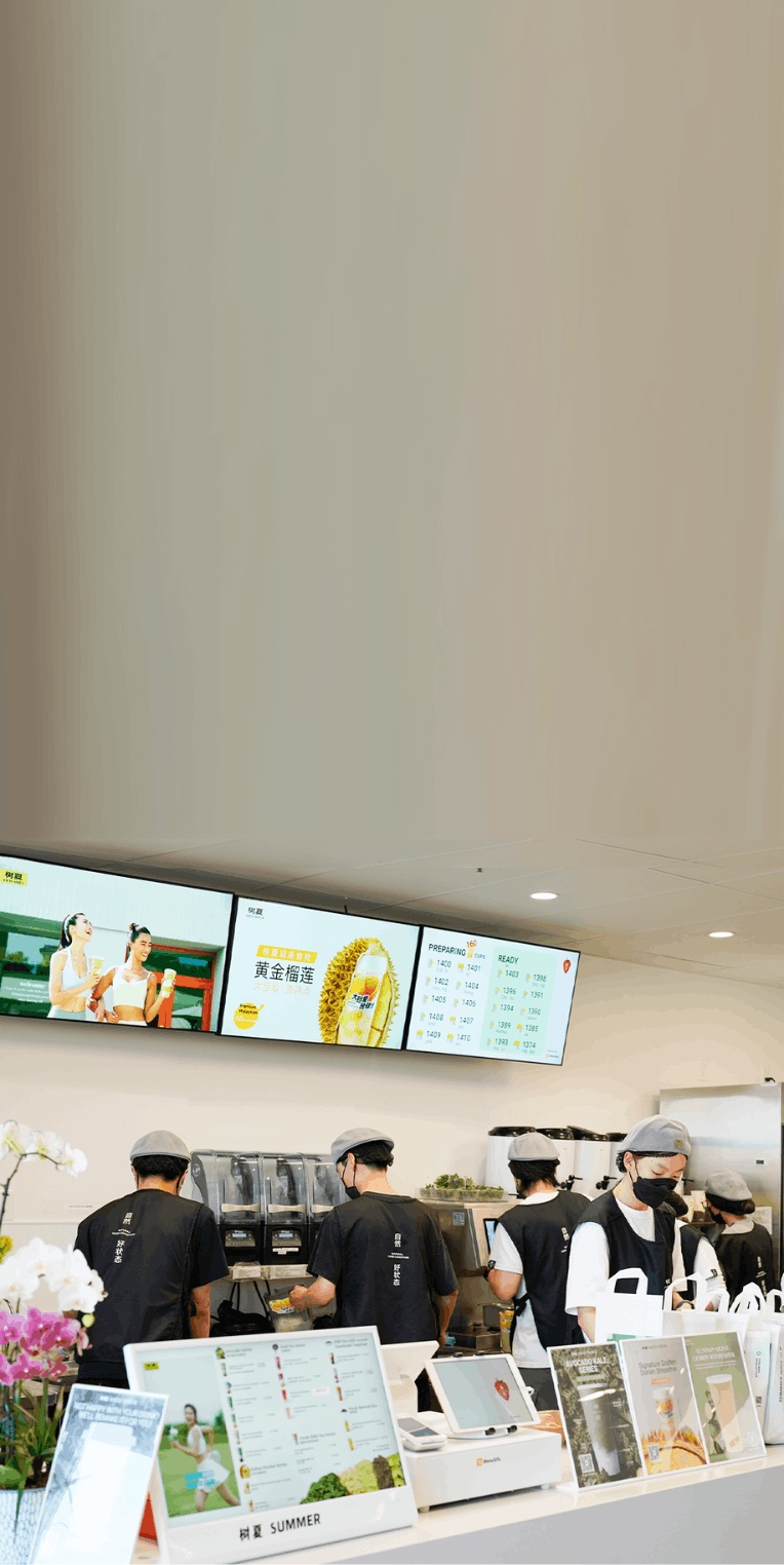 Busy staff in modern bubble tea shop assemble drinks under an order status screen showing real-time updates for customer orders.