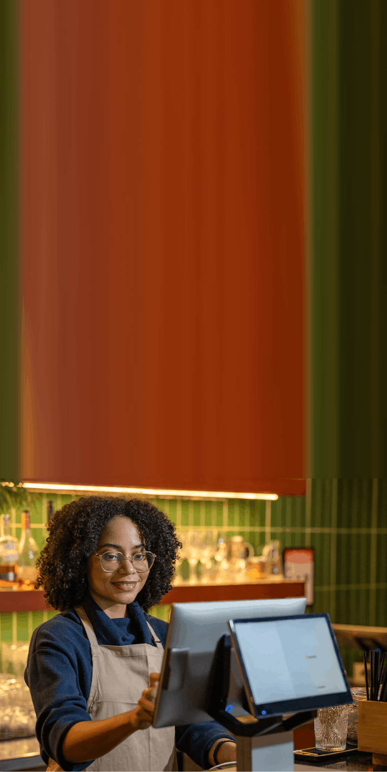 Smiling barista uses a touchscreen point of sale system at a modern café counter.