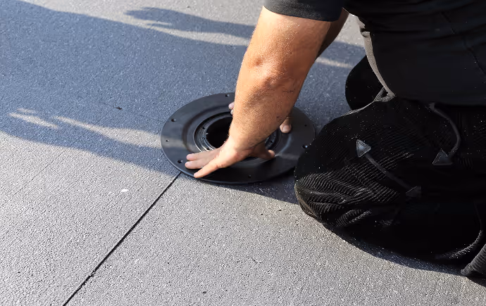 Eine Person installiert einen runden Ablauf auf einer grauen Dachfläche.