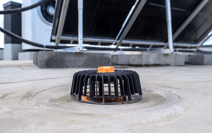 Dachentwässerung mit schwarzem Gitterschutz und orangem Ablassventil auf einem Flachdach.