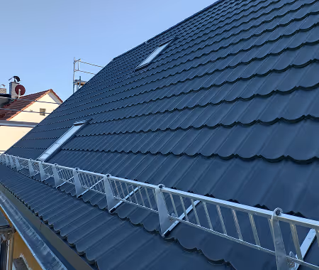 Ein modernes Hausdach mit dunklen Ziegeln und Dachrinnen sowie zwei kleinen Dachfenstern bei klarem Himmel.