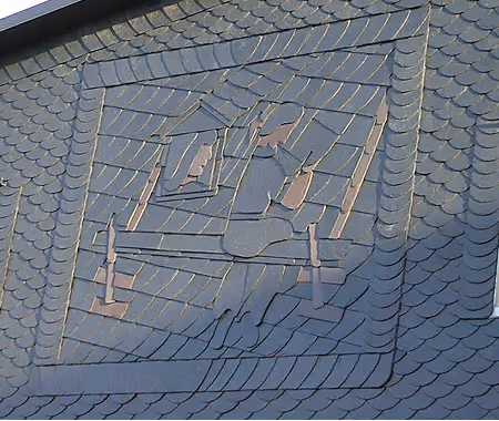 Ein Schieferdach mit einer kunstvollen Gravur, die zwei Handwerker bei der Arbeit zeigt.
