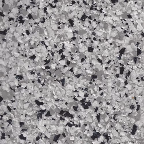 Close-up of a textured epoxy floor coating with white, gray, and black flakes scattered on a gray base.