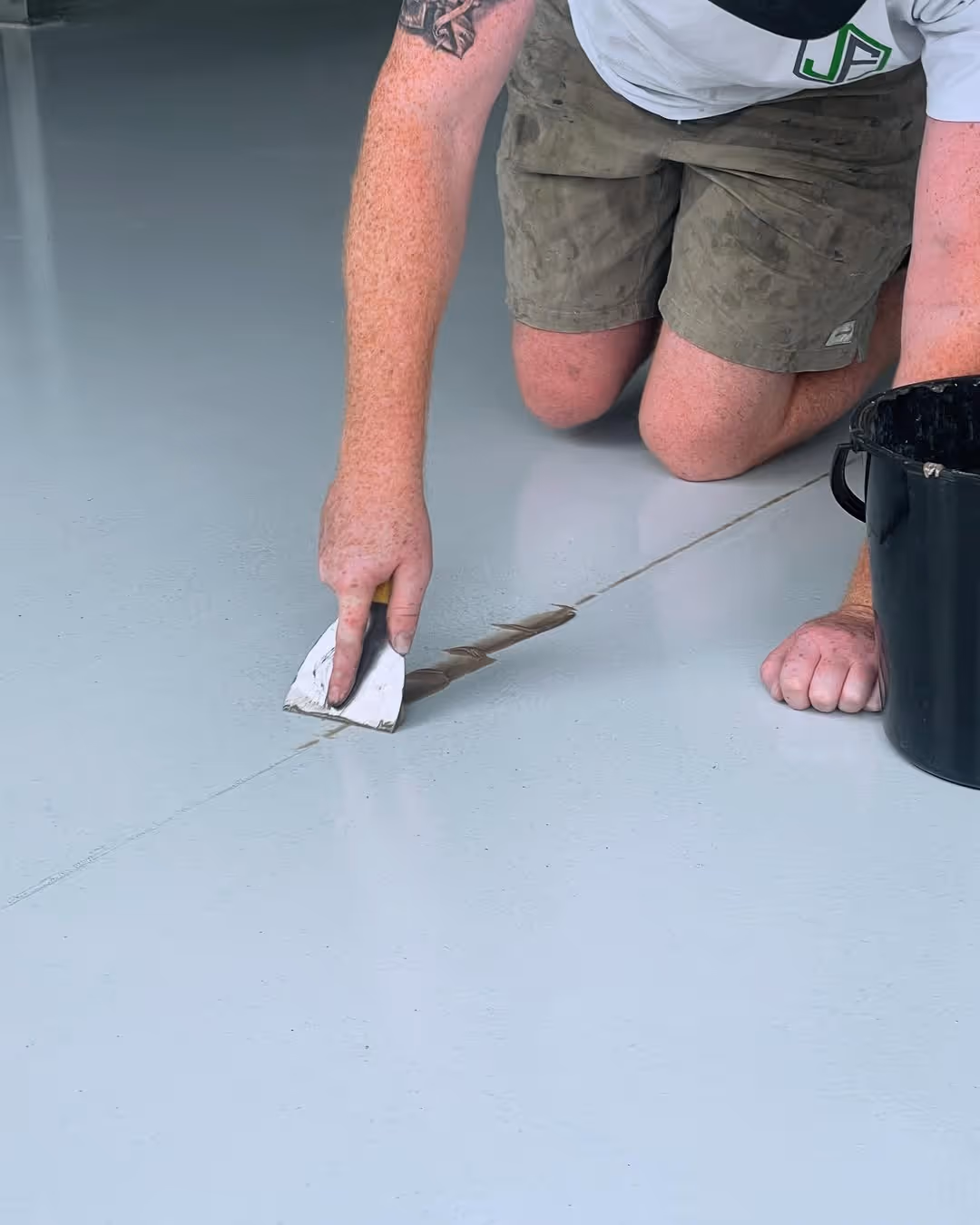 Person kneeling and using a putty knife to apply concrete filler into a crack on a smooth gray floor.